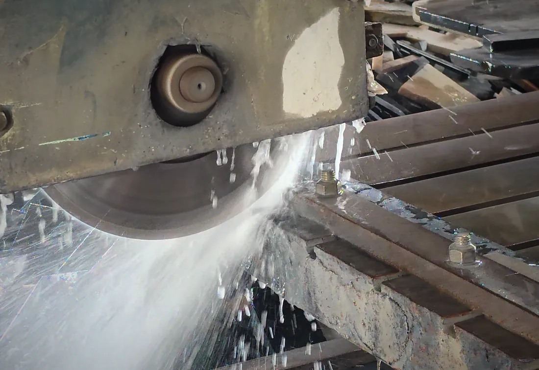 The bridge saw cutting a stone slab, water spraying across the blade to cool it.